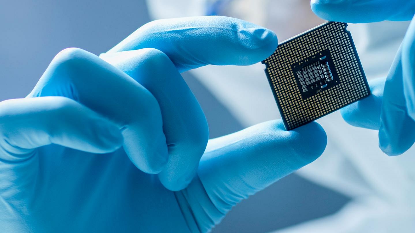 Electronics manufacturing worker in a clean suit inspecting an electronic chip